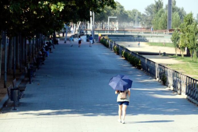 Una dona camina amb un paraigua pel carrer Jaume II de Lleida, vora la canalització del riu Segre, durant l'onada de calor.