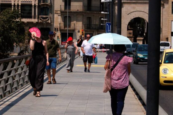 Vianants que caminen pel pont Vell de la ciutat de Lleida es protegeixen del sol amb paraigües, gorres i ventalls.